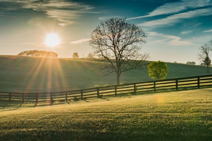 Sun over grass field with fence in foreground