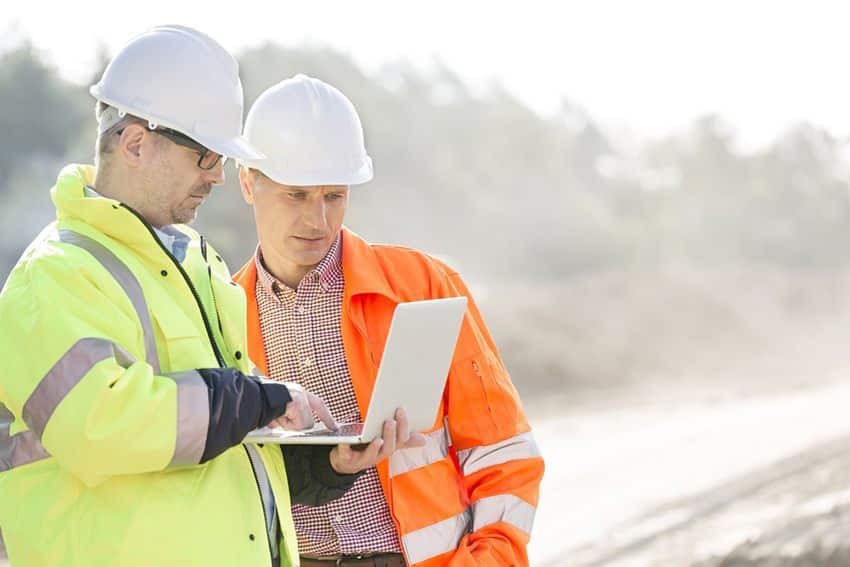 A photo of two construction workers looking at a laptop